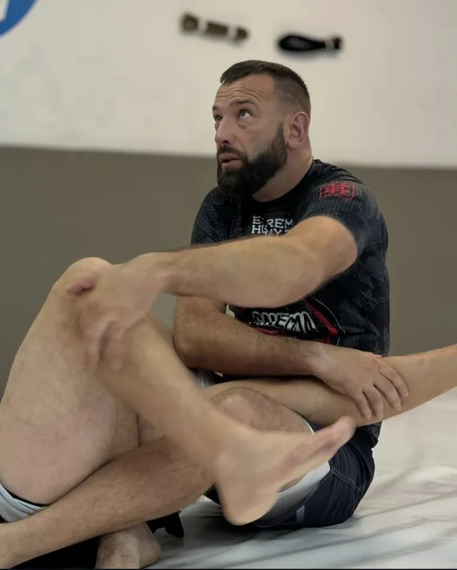 Arek siedzi na macie i trzyma nogę partnera w dźwigni